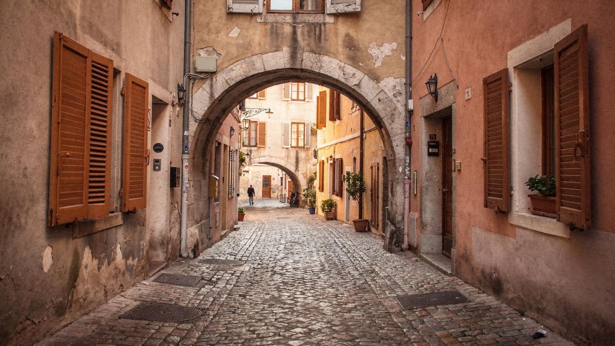 Narrow cobbled lane in a European old quarter with terracotta shutters and an arched passage